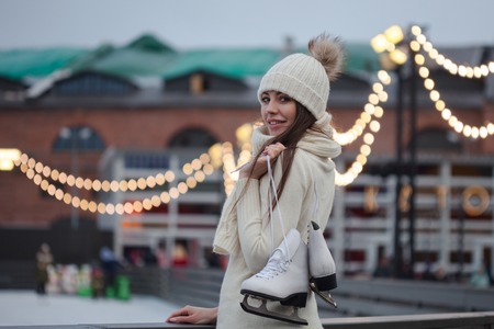 Charming young woman in the Park near the ice rink. Happy young woman in knitted sweater and hat is going skatingの写真素材