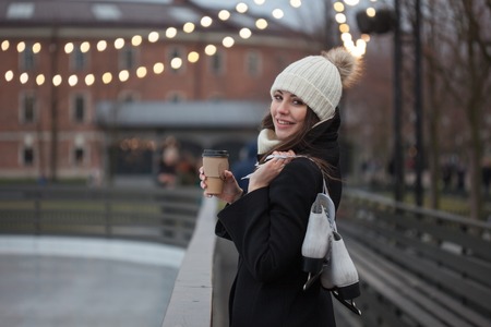 Young brunette with skates on her shoulder, on a background of winter city Park , ice rink