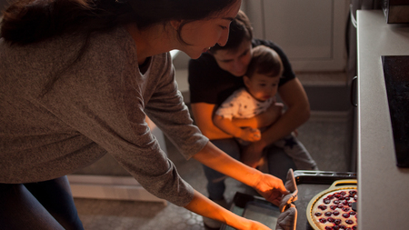 young multiethnic family making a cake together. Mom dad and son pull the cake out of the ovenの写真素材