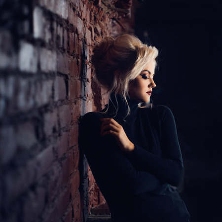 Attractive young blonde in black turtleneck. Beautiful woman with stylish make-up. Sensual portrait in dark tones.の写真素材