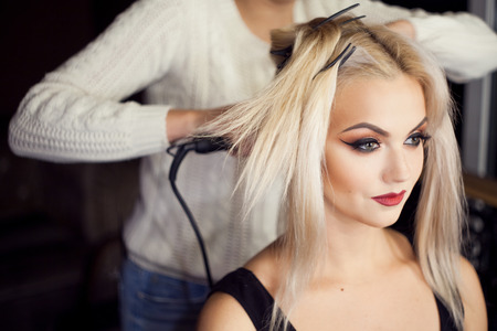 Beautiful young blonde. Makeup artist makes hair. Close-up dark backgroundの写真素材