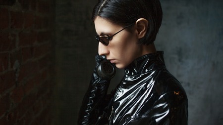 Girl hacker in black leather with retro phone. Young woman in matrix style suit, digital Internet technology and telecommunications, conceptの写真素材