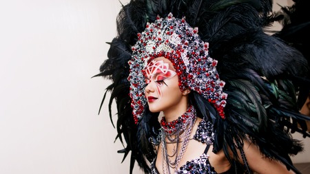 Portrait of a young beautiful woman in a creative look. The style of carnival and dancing. Girl in a headdress with feathersの写真素材