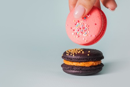 Beautiful bright macaroons. Sweet almond French dessert. Stack of macaroons, Woman's hand takes one cookie, blue backgroundの写真素材