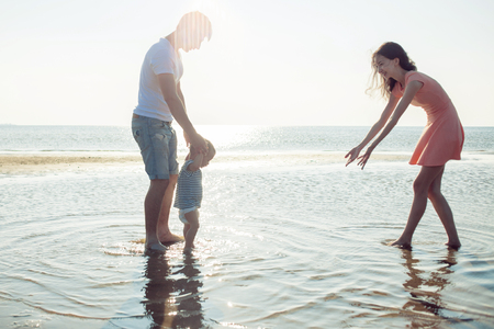 Mom and dad teach baby to walk. Young happy family walking on the beachの写真素材