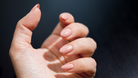 Nude manicure with gold decor. Womens hands close up on black table background