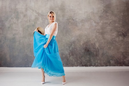 Beautiful young woman in a lush blue skirt, whirling and dancing. Summer style, straw hat with black...