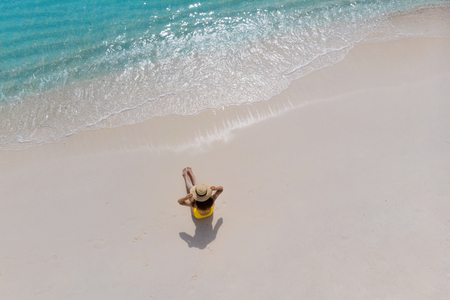 Girl alone on seashore and enjoys the sun. Young woman in a straw hat and a yellow swimsuit, view from the topの写真素材