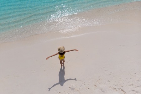 Girl alone on seashore and enjoys the sun. Young woman in a straw hat and a yellow swimsuit stands...