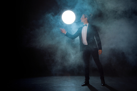 lonely Young man in a suit pulls his hand somewhere and waits for someone. Dark mystical background with smokeの写真素材