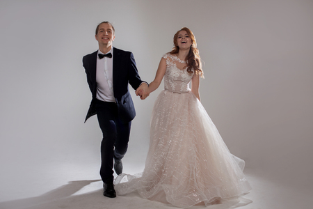 Happy young couple laughing and dancing together. The couple in the Studio a light background. Boyfriend and girlfriend, costume and wedding dressの写真素材