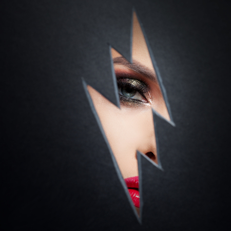 Beautiful female eye with color makeup. Cutout in paper in the form of a lightning. Free space