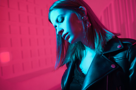 Beautiful girl in retro wave on the neon light. Fashion portrait of trendy young woman in leather...