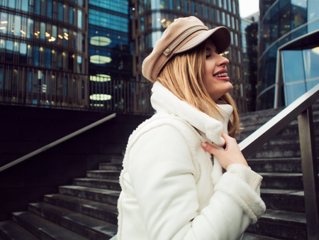 Stylish and elegant young woman on the background of the business center. Beautiful girl in white jacket and cap, walkの写真素材