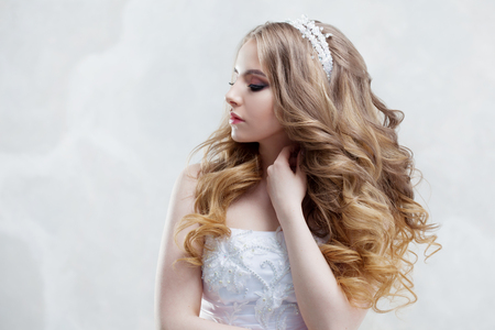 Charming young bride with luxury hairstyle. Beautiful woman in wedding dress. Hairstyle with fluffy curls. Portrait on light backgroundの写真素材