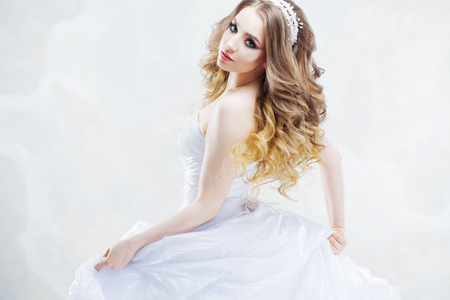 Charming young bride with luxury hairstyle. Beautiful woman in wedding dress. Hairstyle with fluffy curls. Portrait on light backgroundの写真素材