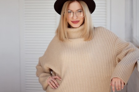 Stylish and beautiful young blonde in black felt hat and beige oversize sweater. Young woman with...