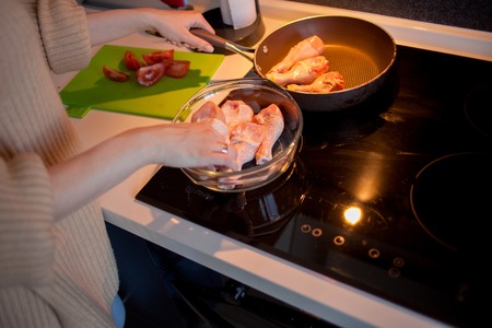 Beautiful young blonde cooks chicken with vegetables, self-cooking healthy food. Beautiful charming woman in her apartmentの写真素材