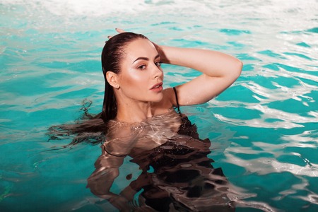 beautiful girl portrait in the pool. Young woman swimming in water. Portrait of a beautiful brunette with wet hairの写真素材
