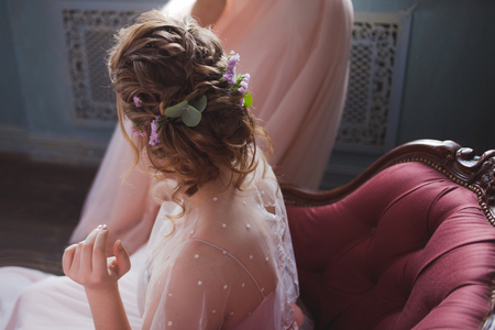 Beautiful and elegant wedding hairstyle. Young bride sitting in a chair, back viewの写真素材