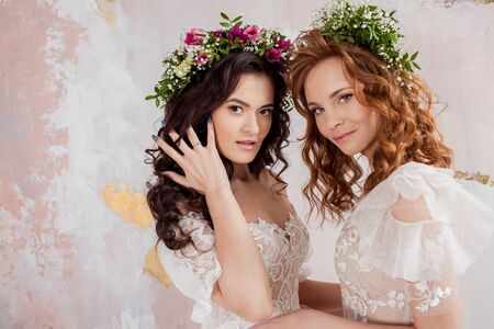 Two charming brides in beautiful spring wreaths on their heads. Beautiful young women in wedding dresses, Studio portraitの写真素材