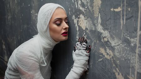 Mummy girl pressed against the wall, eavesdropping. Portrait of a young beautiful woman in bandages...