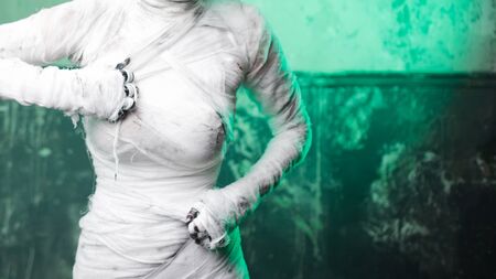Glamorous mummy. Portrait of a young beautiful woman in bandages all over her body. Halloween or plastic surgery concept, Green light, mummy breaks into the bandages themselvesの写真素材