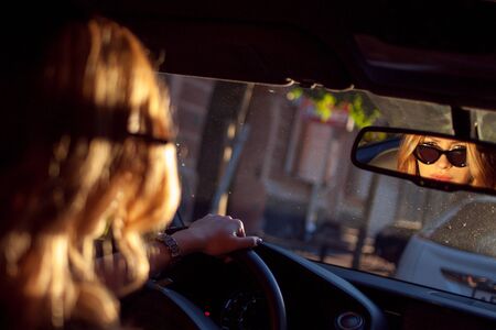Beautiful young woman in sunglasses sitting behind the wheel of a car. Photo from the back seat....