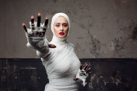 Beautiful young woman in bandages. Girl in a mummy costume, Pulling hand. Halloween or plastic surgery conceptの写真素材
