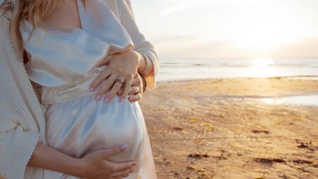 Romantic walk on the beach, waiting for a baby. Happy young couple hugging tummy, spending time by...