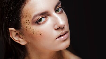 Charming girl with trendy glitter makeup, fashionable make-up with gold glitter on the cheekbones and near the eyes.の写真素材