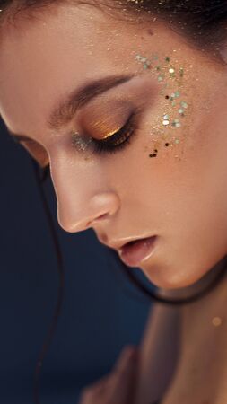 Charming girl with trendy glitter makeup, fashionable make-up with gold glitter on the cheekbones and near the eyes.の写真素材