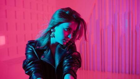 Beautiful girl dancing in retro wave on the neon light. Fashion portrait of trendy young woman in leather jacket, blue and purple light on her faceの写真素材