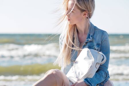 Young cheerful girl on the seashore. Young blonde woman smiling. Young cheerful woman on a walk, denim jacket and Trendy beige skirtの写真素材