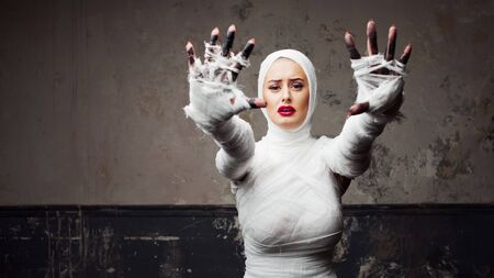 Beautiful young woman in bandages. Girl in a mummy costume, Pulling hand. Halloween or plastic surgery conceptの写真素材