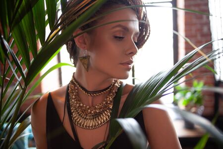 Tropical flavor. Close-up portrait of a young beautiful, exotic woman with large jewels and afro braids hairstyle , surrounded by tropical plants, close to the face.の写真素材