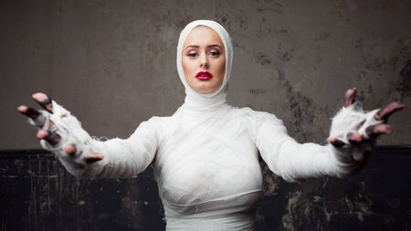 Beautiful young woman in bandages. Girl in a mummy costume, Pulling hand. Halloween or plastic surgery conceptの写真素材