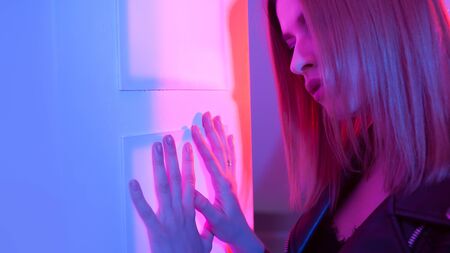 Futuristic style portrait in blue and purple light. Trendy young woman in leather jacket applies palm to enter, Fingerprint identification, conceptの写真素材