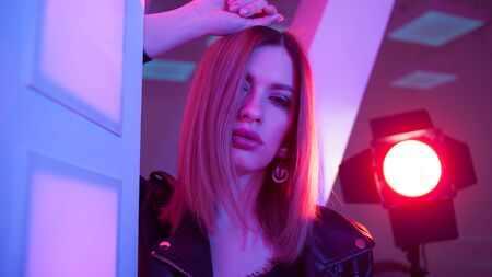 Futuristic style portrait in blue and purple light. Fashion portrait of trendy young woman in leather jacket, Pink color light on a background and her faceの写真素材