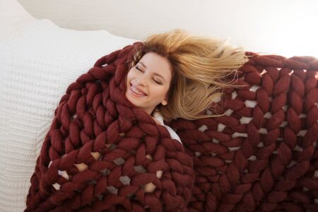 Cute young blonde lying on the bed wrapped in a soft cozy blanket. Warmth and comfort of home, conceptの写真素材