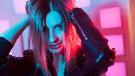 Futuristic style portrait in blue and purple light. Fashion portrait of trendy dancing young woman in leather jacket, Pink color light on a background and her faceの写真素材