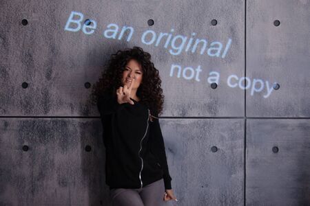 Curly young woman actively posing on a concrete wall background. A colored illuminated inscription...