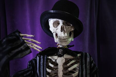Funny human skeleton in a jacket and bowler hat. Halloween, skeleton waving cheerfullyの写真素材