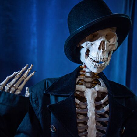 Funny human skeleton in a jacket and bowler hat. Halloween, skeleton waving cheerfully