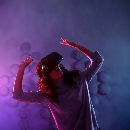 Virtual reality game. A girl in a virtual reality helmet plays a game or explores the environment. Portrait in neon light, retrowave styleの写真素材