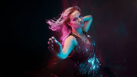 Attractive dancing blonde in the club, neon light, motion effects. Black background, long exposure