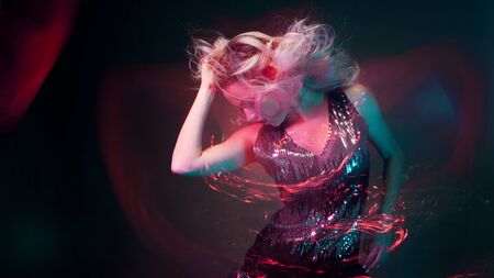 Attractive dancing blonde in the club, neon light, motion effects. Black background, long exposureの写真素材