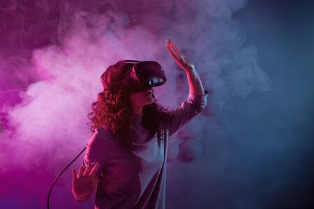 Virtual reality game. A girl in a virtual reality helmet plays a game or explores the environment. Portrait in neon light, retrowave styleの写真素材