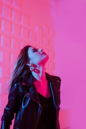 Beautiful girl dancing in retro wave on the neon light. Fashion portrait of trendy young woman in leather jacket, blue and purple light on her faceの写真素材