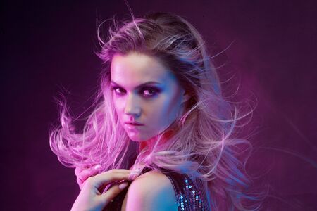 Young attractive blonde woman dancing in club, color light, motion effects. Black background, long...
